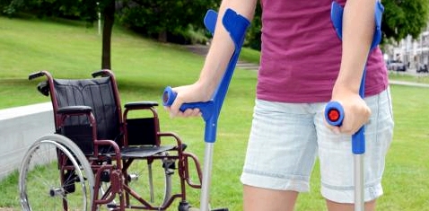 Frau mit Krücken vor Rollstuhl