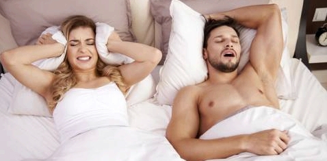 Eine Frau liegt neben ihrem schnarchenden Mann im Bett und kann nicht schlafen