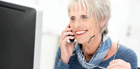 Eine ältere Frau telefoniert vor einem Computer