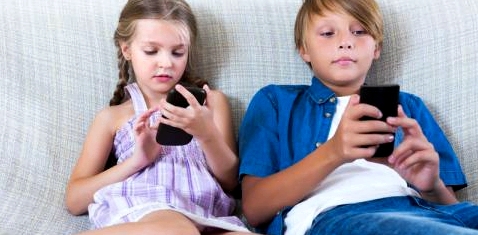 Zwei Kinder sitzen nebeneinander und blicken auf ihre Smartphones