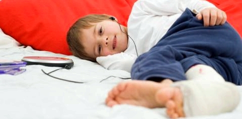 Ein Junge liegt mit Gipsbein im Bett uns hört Musik