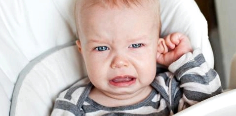Ein Baby weint und hält sich das Ohr