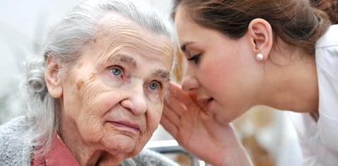 Eine Pflegerin spricht einer alten Frau ins Ohr