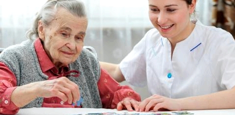 Eine alte Frau puzzelt mit ihrer Pflegerin