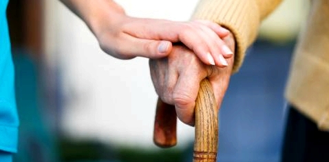 Die Hand einer Pflegerin hält die eines alten Mannes