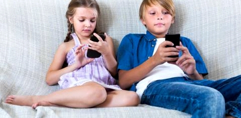 Zwei Kinder sitzen auf einer Couch und spielen mit ihren Handys
